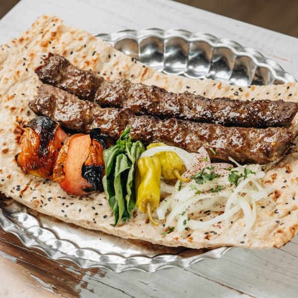 MidEast Eats' koobideh kebabs on flatbread with grilled tomatoes, onions, and peppers.