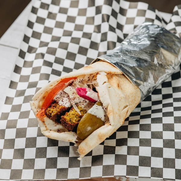 A MidEast Eats falafel wrap, filled with falafel, vegetables, and sauce, on checkered paper.